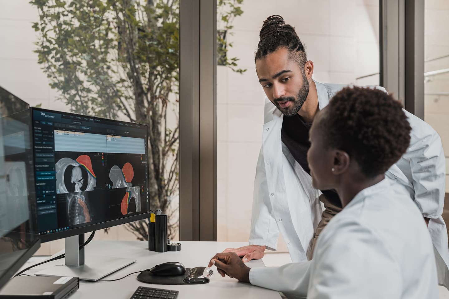 Medical professionals in white coats examining anatomical scans on a computer monitor in a bright office with plants.