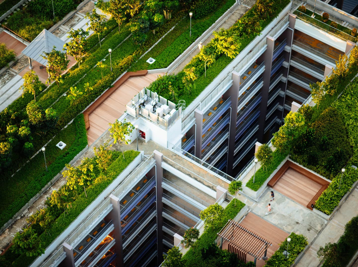 Aerial view of a modern apartment building with extensive rooftop gardens, walkways, and green spaces integrated into the design.