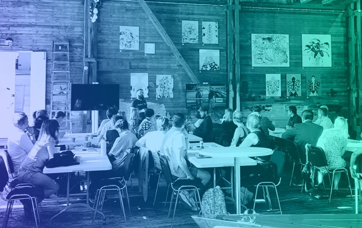People attending a workshop in a wooden barn with artwork displayed on walls, bathed in blue-green lighting.