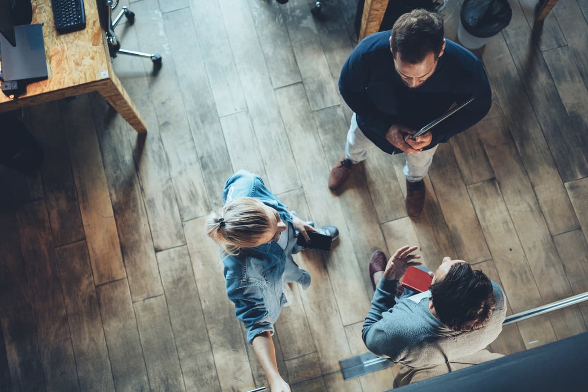 Overhead view of three people having a discussion on wooden flooring in a modern office space.