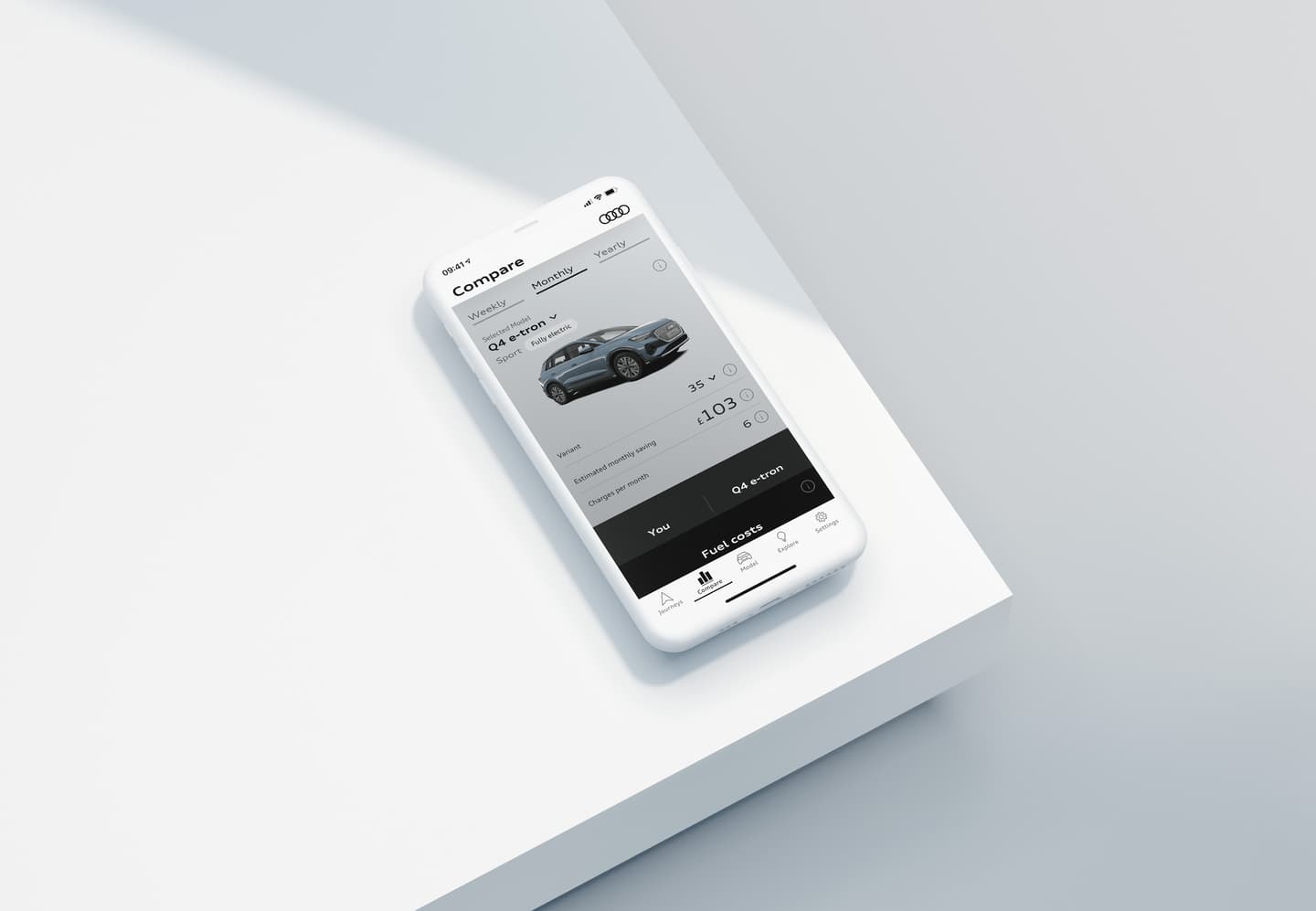 Smartphone displaying Audi app comparing Q4 e-tron vehicle costs and fuel expenses on a white surface.