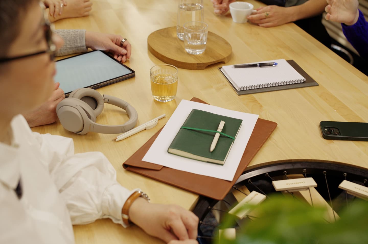 People gathered around wooden table with tablet, notebook, headphones, drinks and stationery during a meeting.