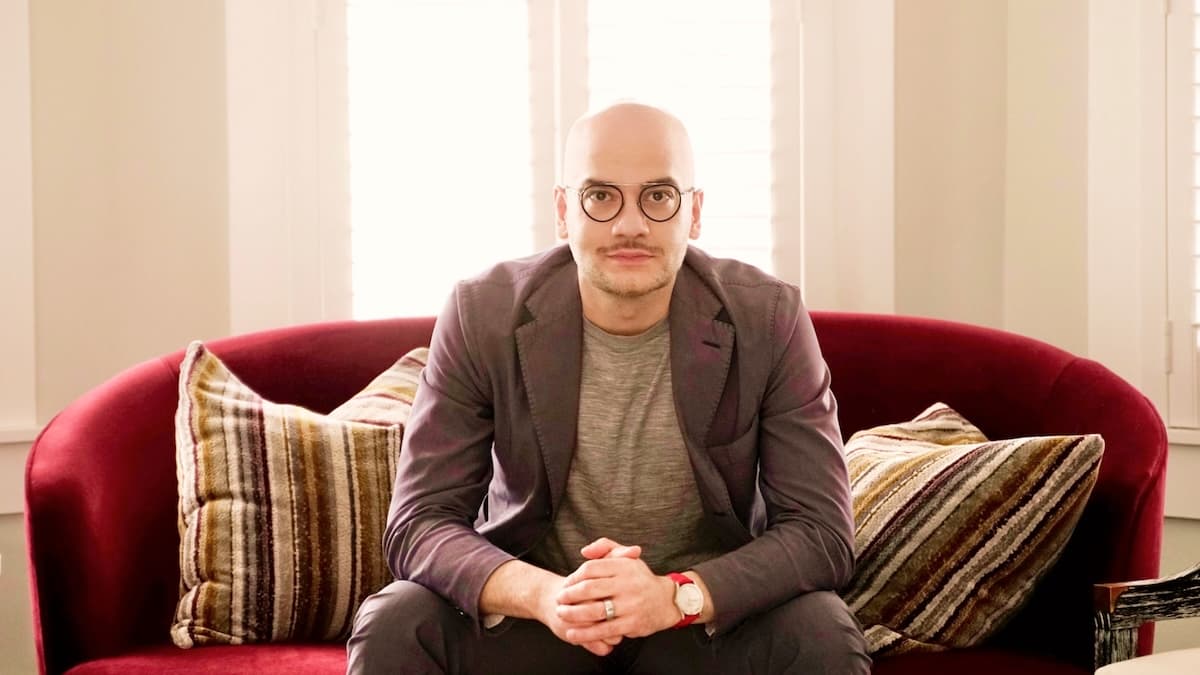 Shwan Lamei of Emulate Energy in a grey blazer seated on red sofa with striped cushions in bright room with white curtains.