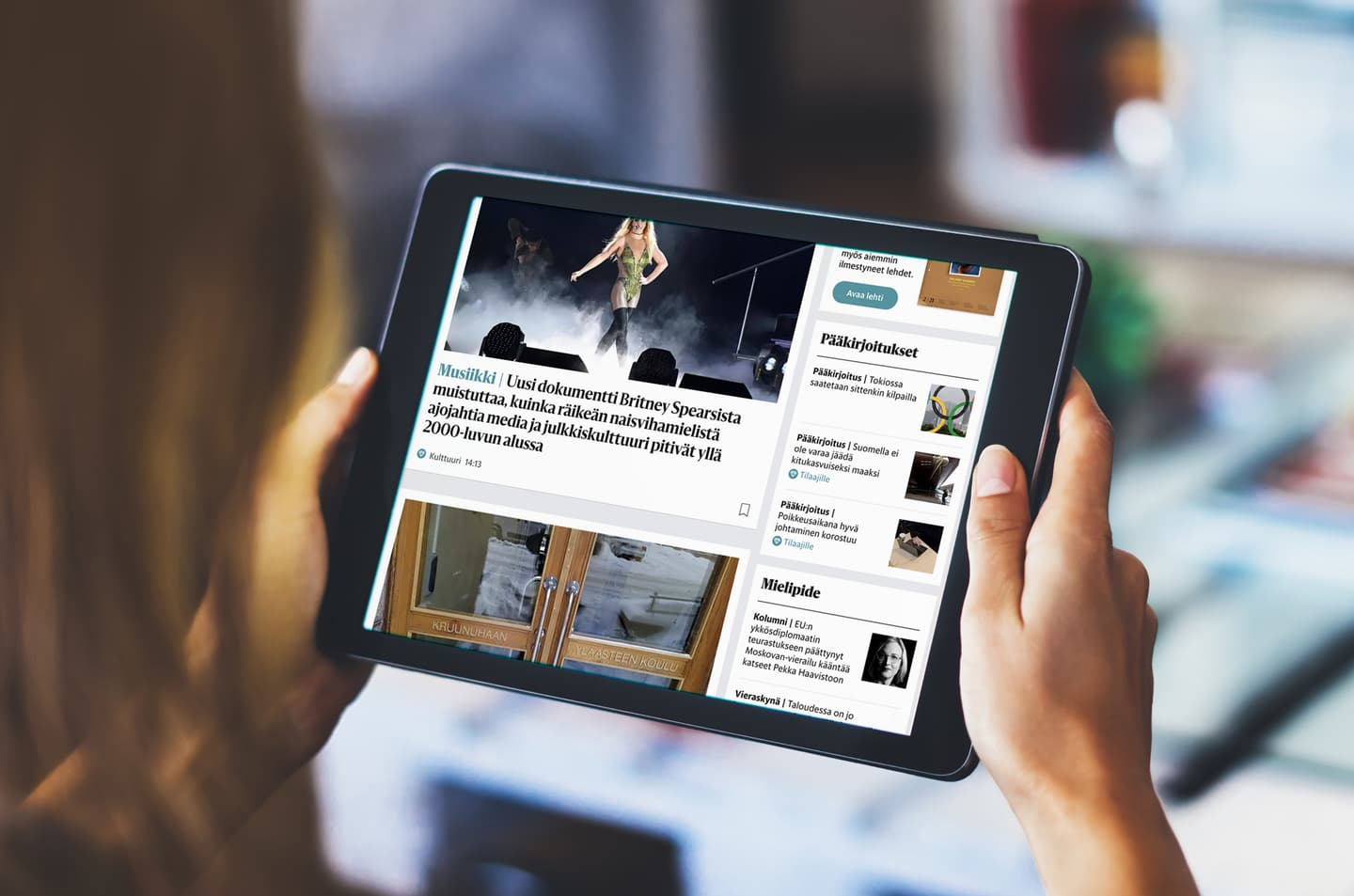 Person holding tablet displaying Finnish news website with entertainment article and various news sections visible.