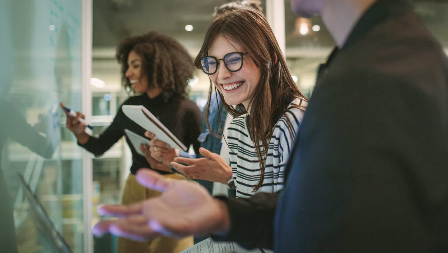 Smiling woman in striped top and glasses collaborating with colleagues in a modern office environment.