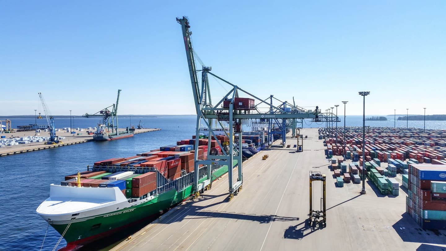 Busy shipping port with cargo vessel loaded with colourful containers, large cranes and stacked containers on the dock.